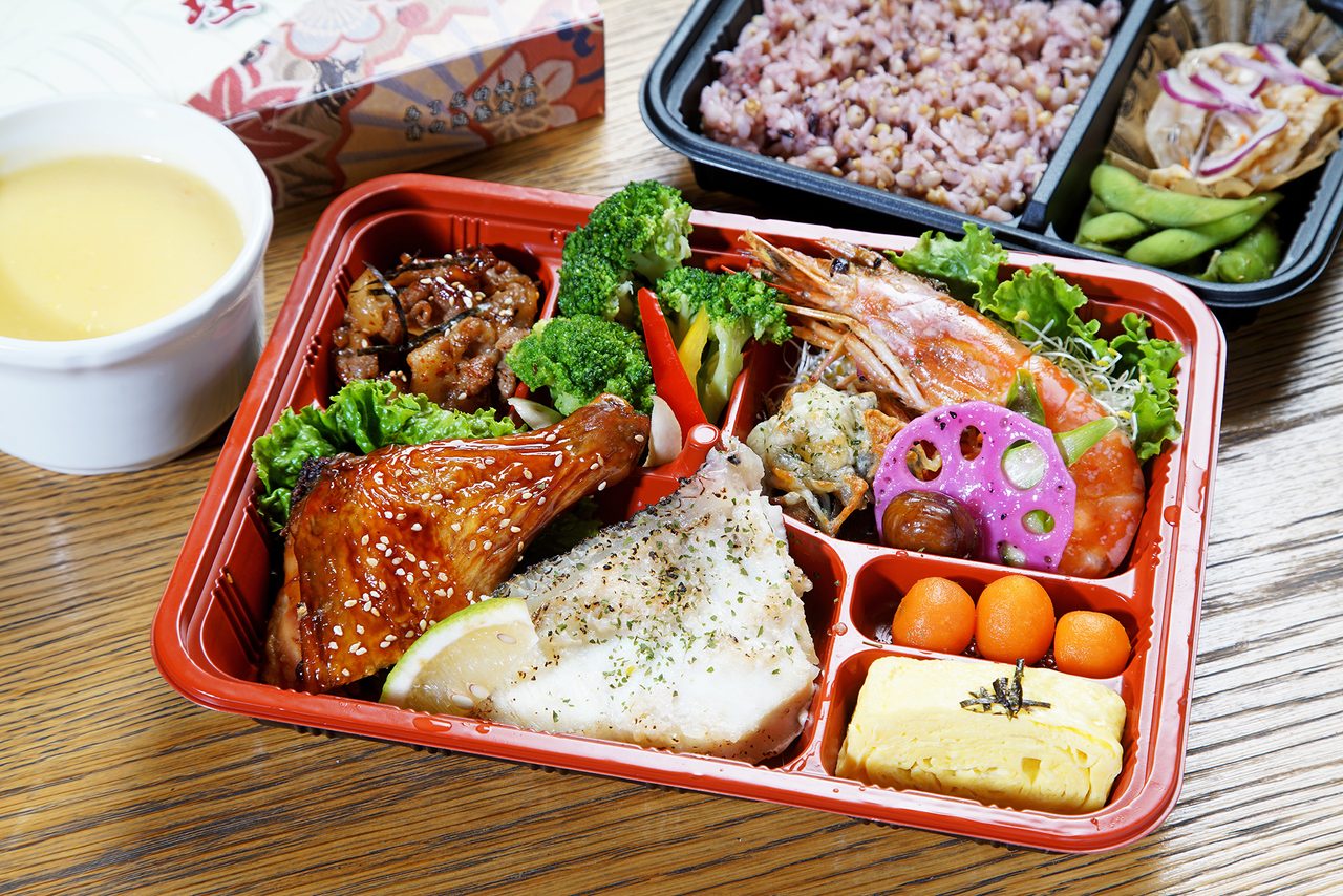 紅黑雙色會議餐盒，盛裝烤雞腿、鮮蝦、玉子燒與紫米飯，旁附一碗濃湯